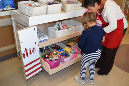 Katie's Kart volunteer, showing cart to young girl at hospital.